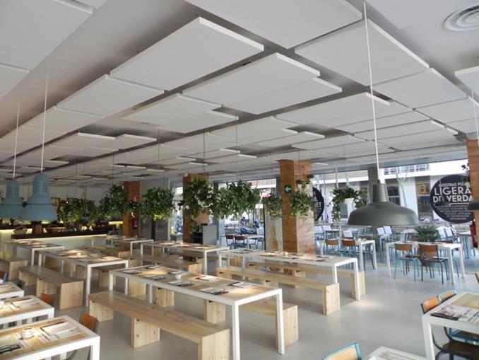Insonorización Acústica en Restaurantes con Techos Tensados Interior de un restaurante con techos tensados acústicos, mesas y bancos de madera, plantas colgantes y luces colgantes.